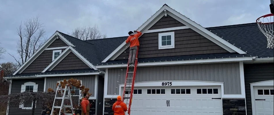 Crew on ladder installing holiday lights on the eaves of house in Grand Rapids, MI.