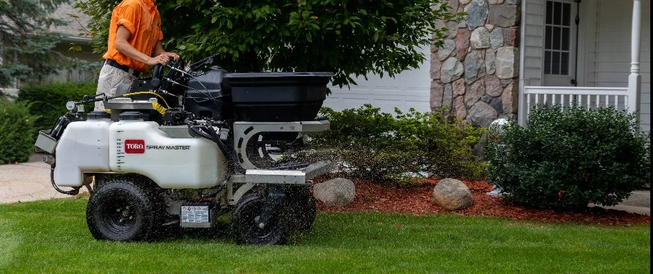 A worker fertilizing a lawn in Plainfield Charter Township, MI, with a granular spreader.
